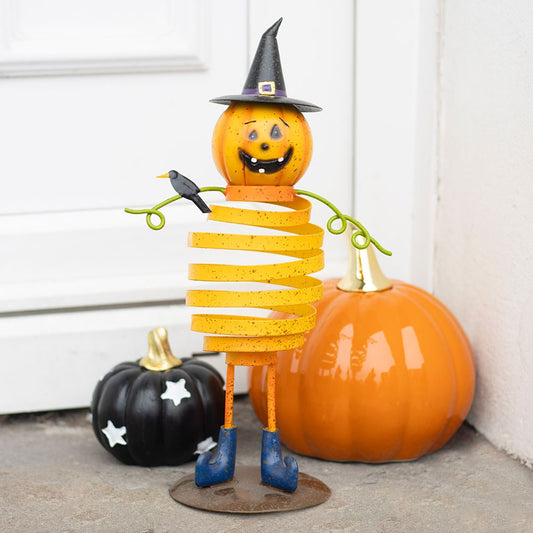Halloween-themed decorative figure with a springy body and pumpkin head, standing next to pumpkins.