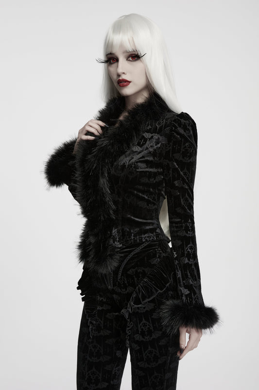 A model with long white hair, dramatic false eyelashes, and red lipstick wears a black velvet bat patterned gothic jacket with black faux fur trim, photographed against a light grey studio background.