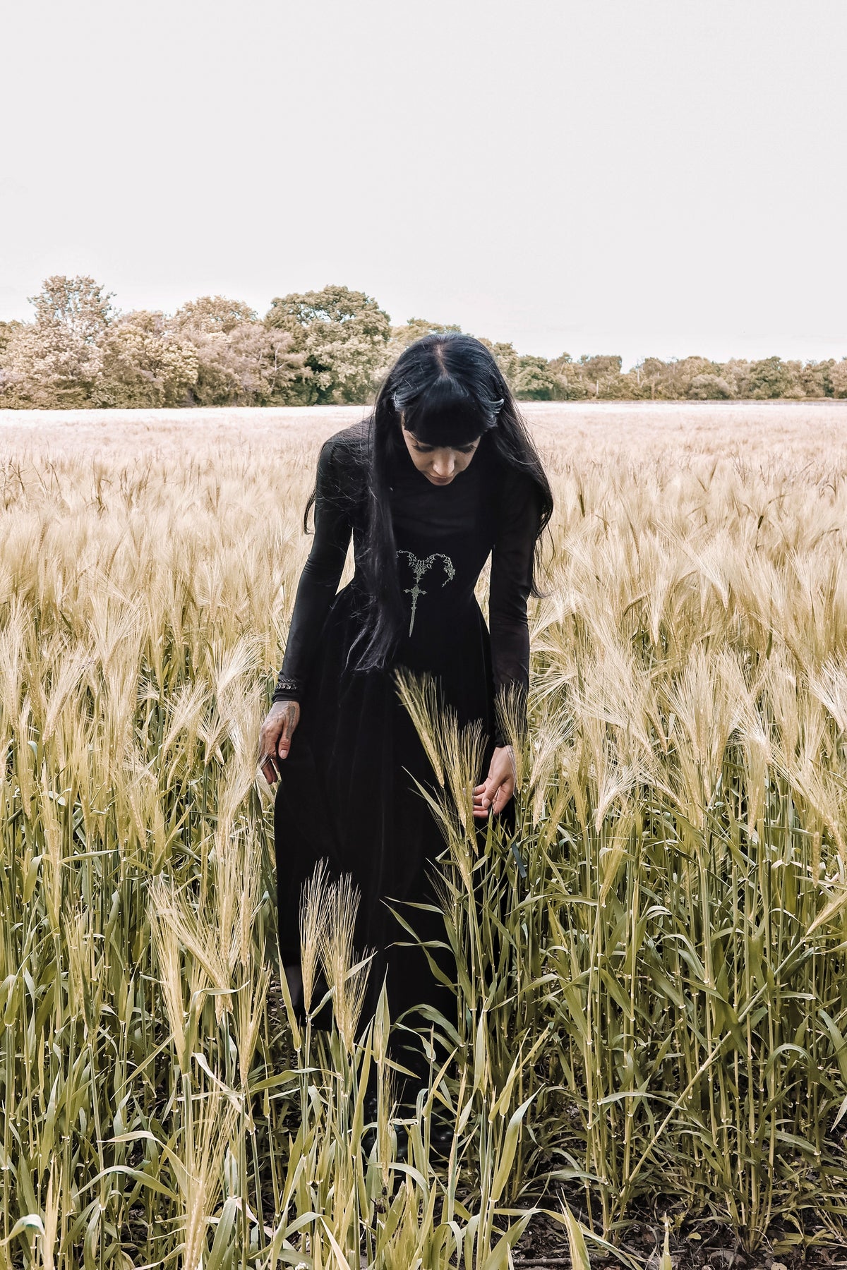 PJ the Heathen alternative model wearing a Dark in Love Gothic Velvet Maxi Dress over a long sleeve top and standing in tall grass