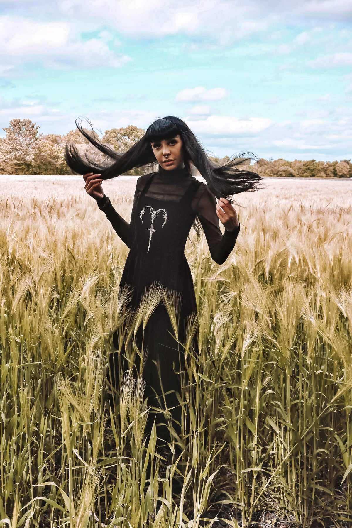 PJ the Heathen alternative model wearing a Dark in Love Gothic Velvet Maxi Dress in a field with a blue sky