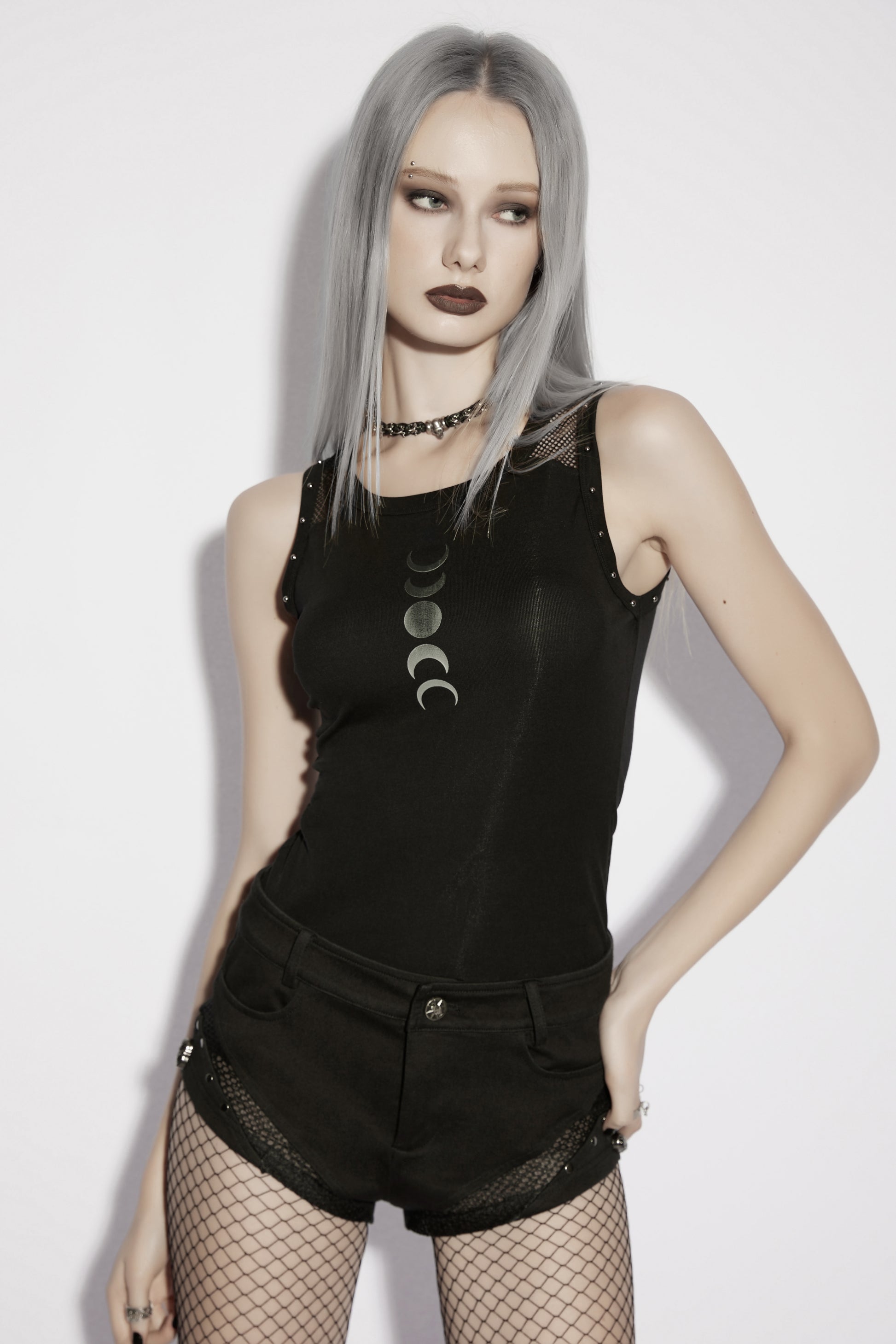 Model wearing a goth moon vest with moon phase print, paired with shorts and fishnet stockings, showcasing alternative fashion style.