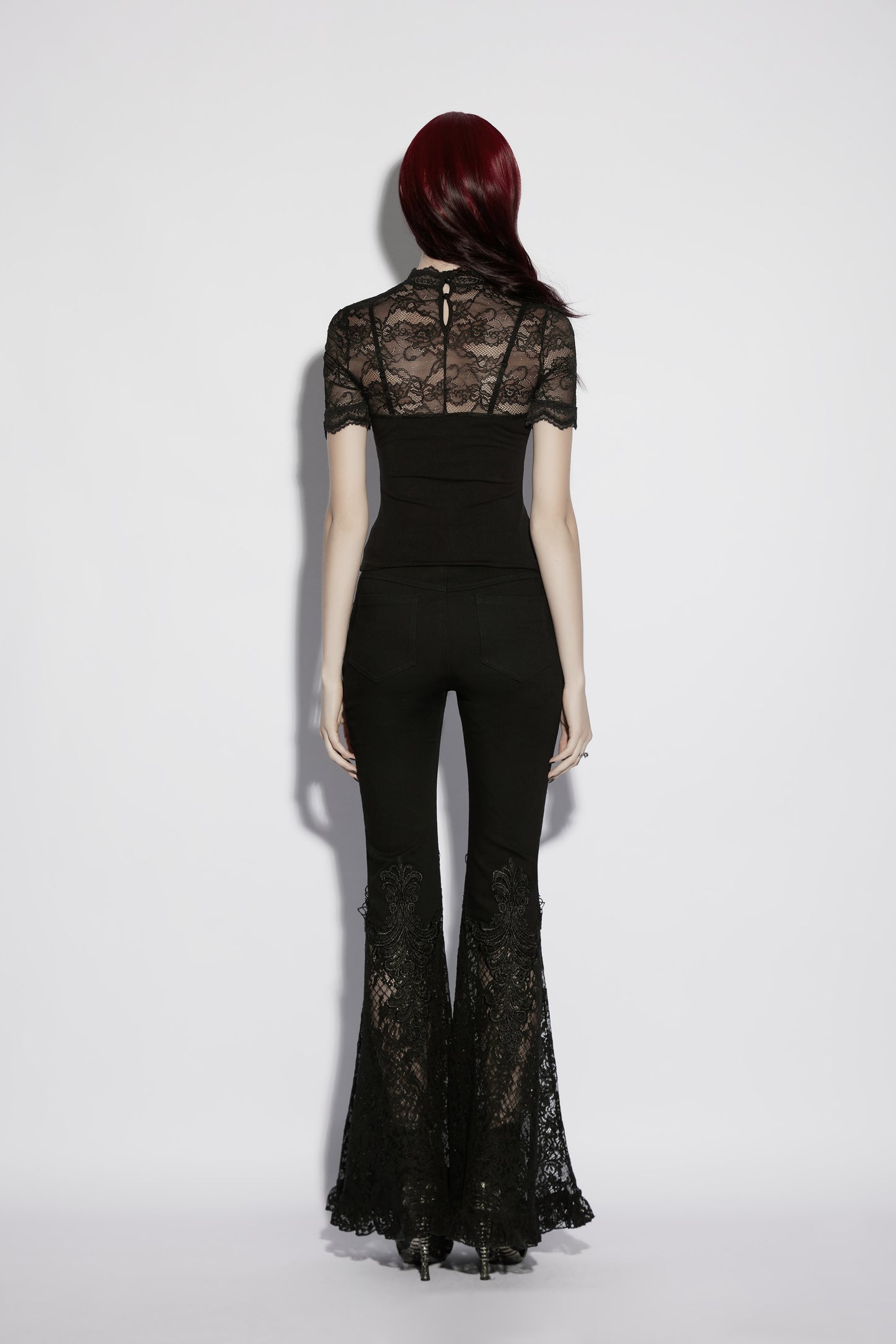 Back view of a model in a black lace panel goth t shirt and flared lace pants.