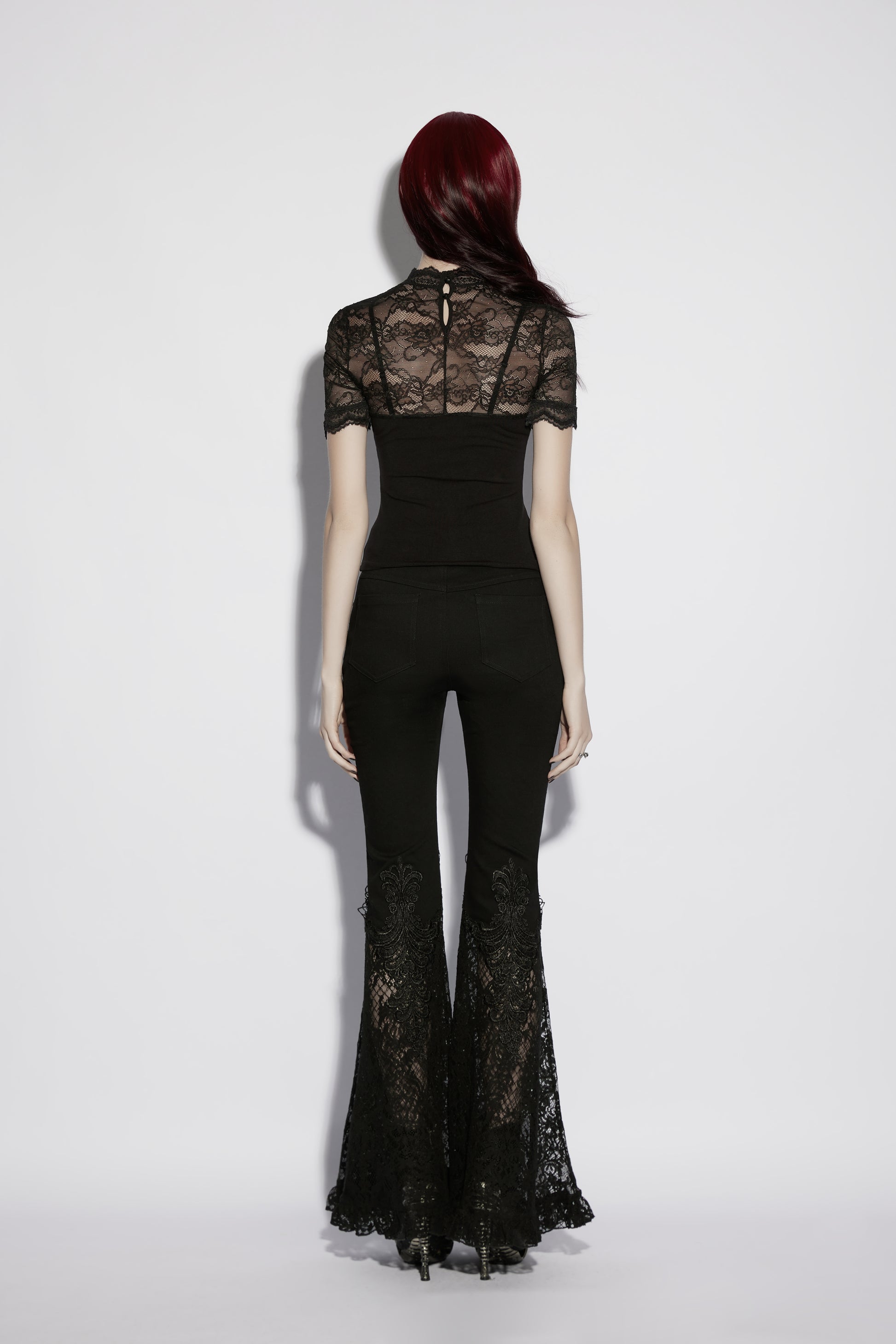 Back view of a model in a black lace panel goth t shirt and flared lace pants.