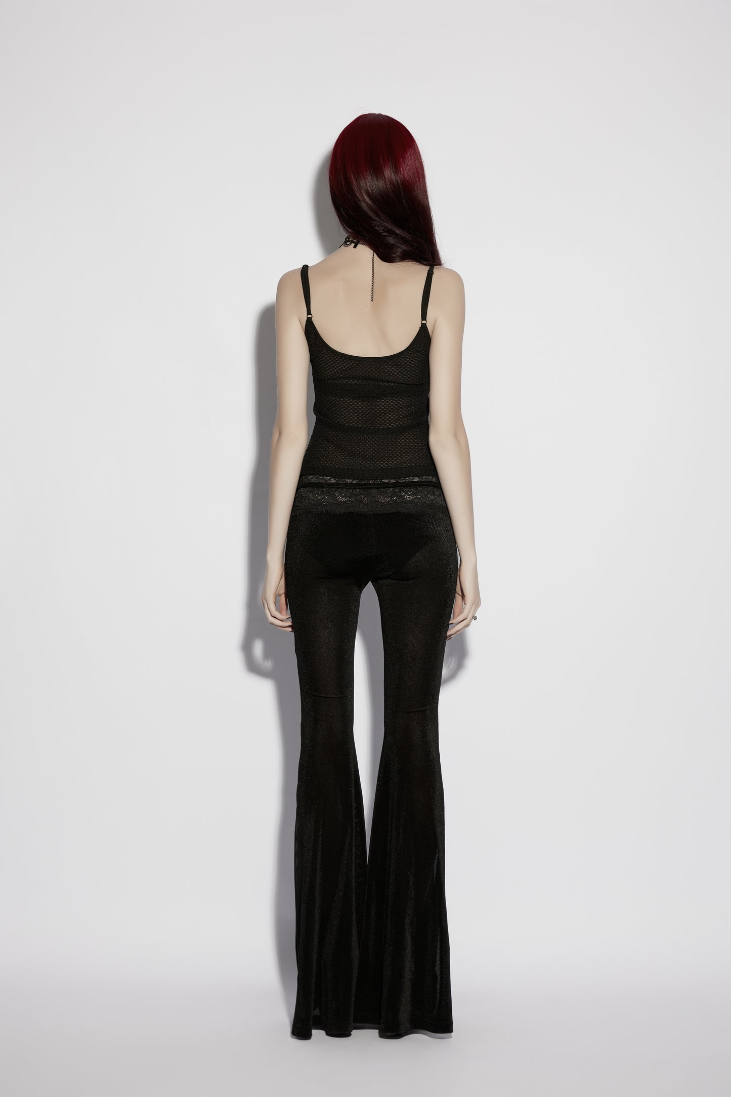 Back view of a model wearing a mesh goth camisole paired with flared black pants, showcasing gothic style.