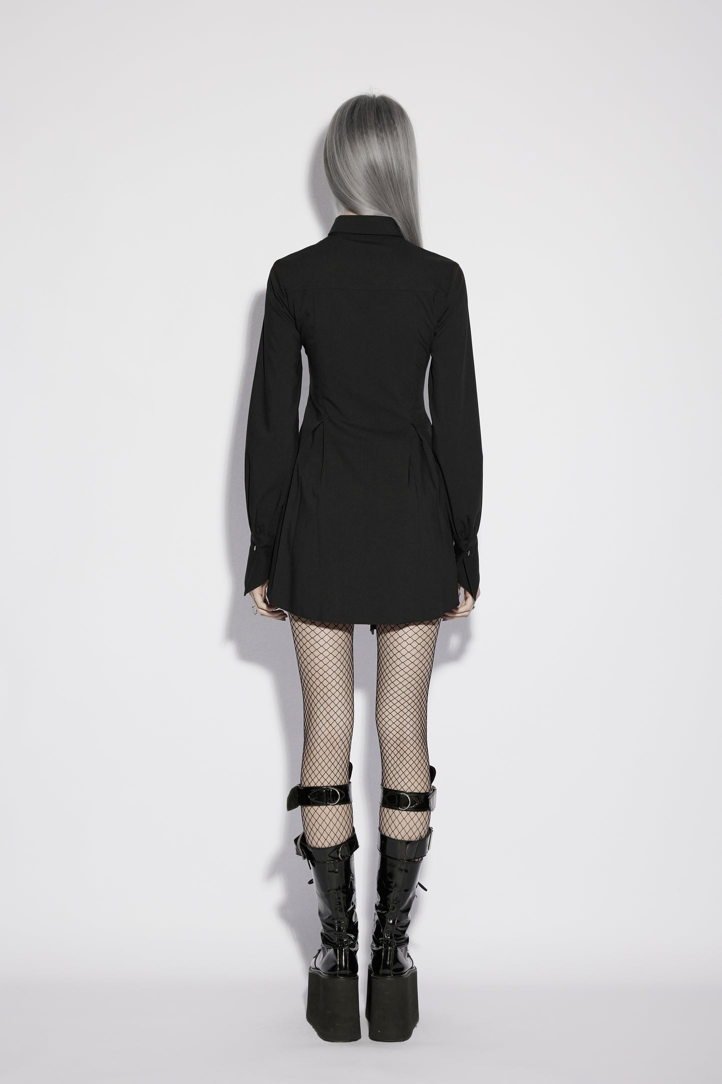 Back view of a model wearing the Punk Rave Nyx Asymmetrical Shirt Dress with fishnet tights and platform boots.