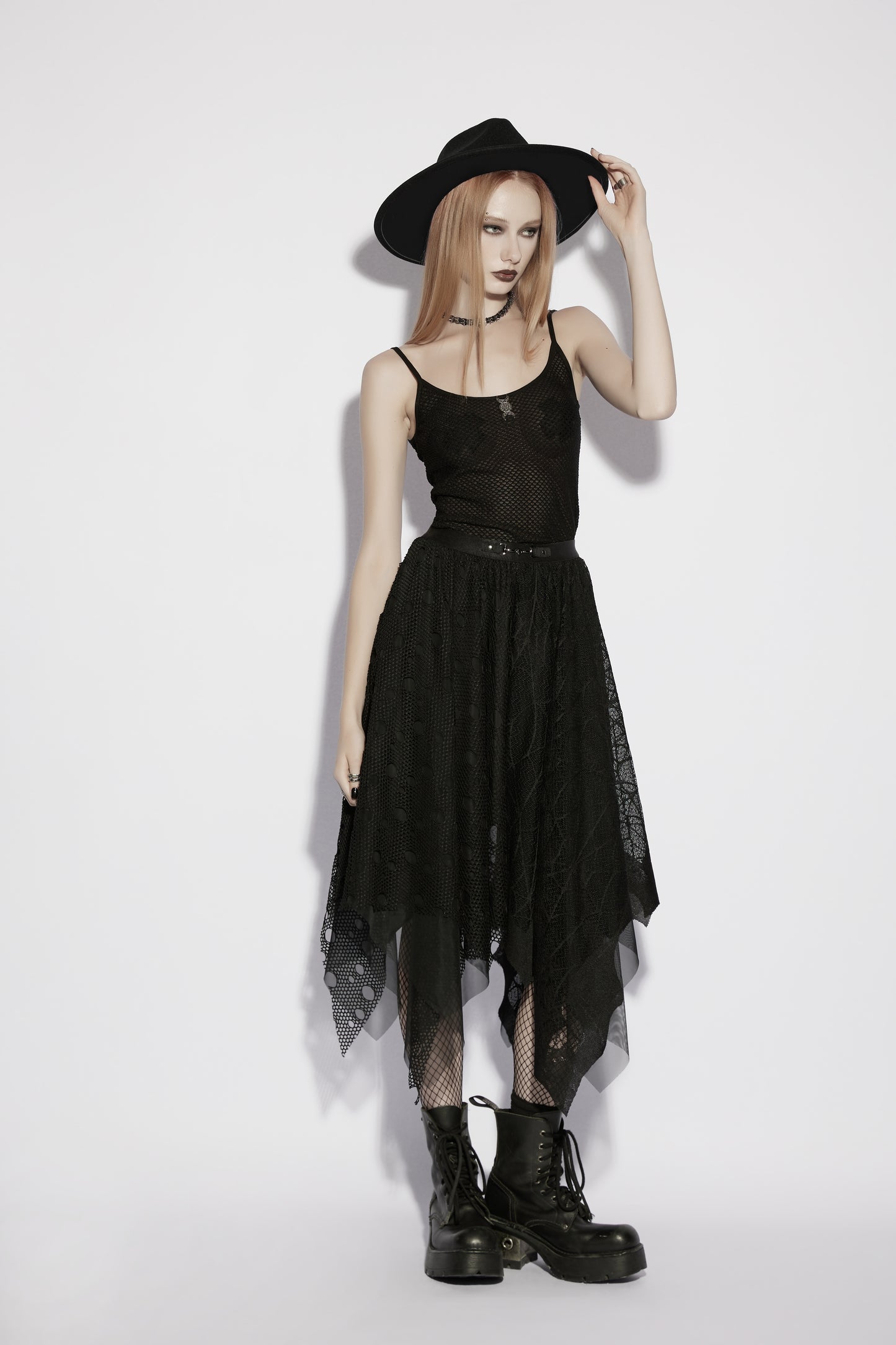 Model wearing a mesh goth camisole and black skirt with a hat and boots, showcasing a punk rave style.