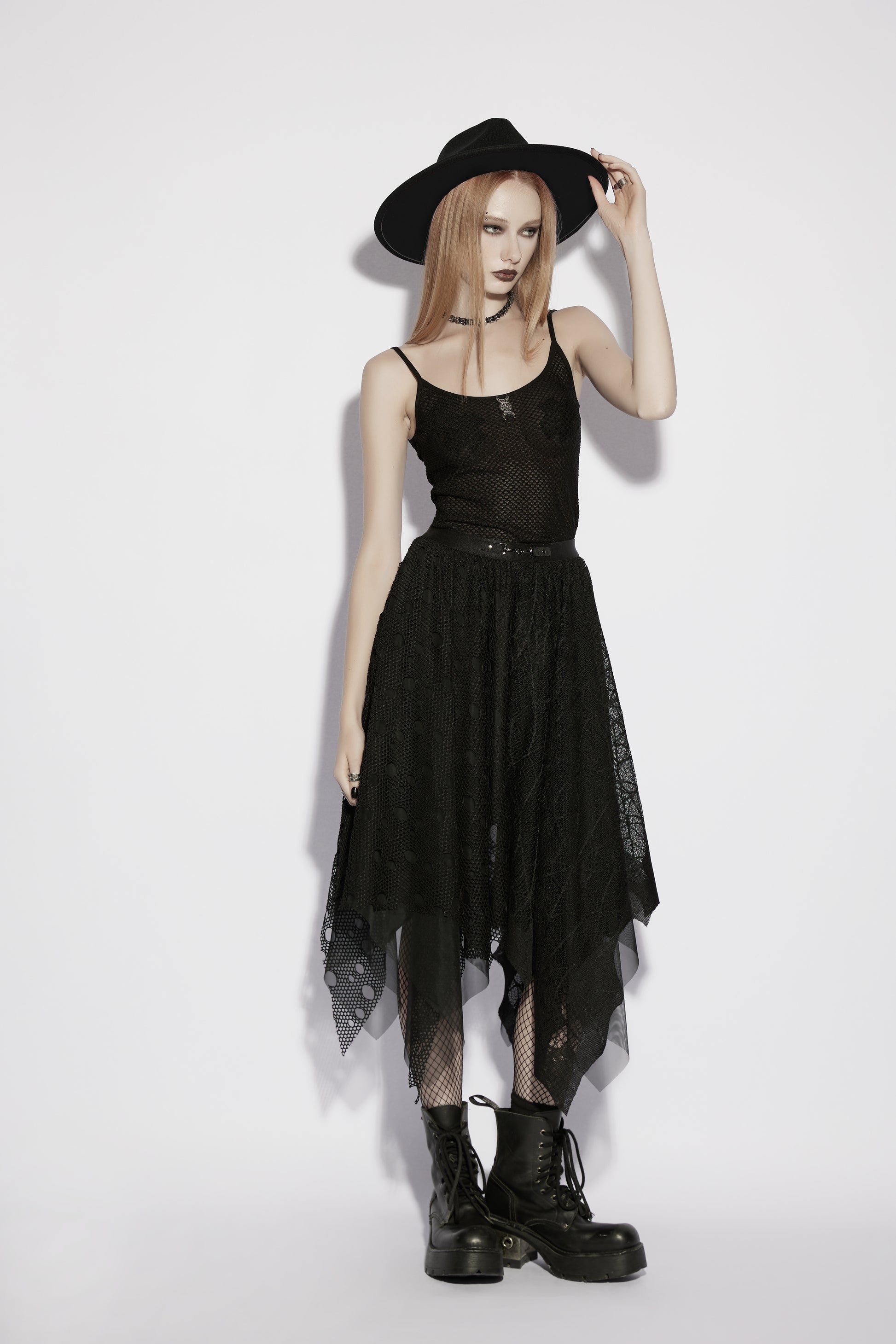 Model wearing a mesh goth camisole and black skirt with a hat and boots, showcasing a punk rave style.
