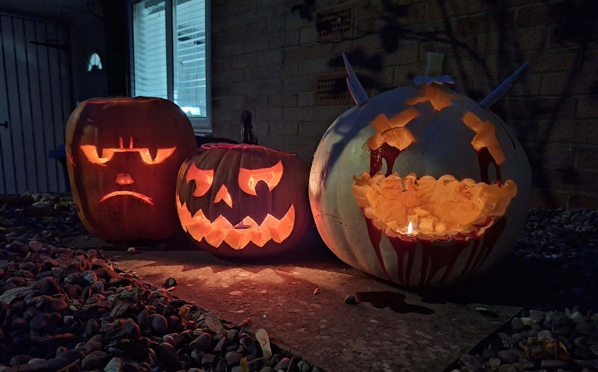 Three carved Halloween pumpkins with glowing lights on a dark outdoor ground.