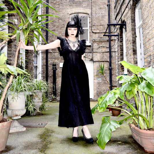 Julia Rose wearing the Punk Rave Elowen Goth Romantic V-Neck Flying Sleeve Dress stood in a courtyard surrounded by plants in pots